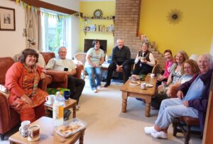 The Mayor attending the St Leonard's Vicarage Tea Party, sitting in the lounge with the vicar and other guests, enjoying a cuppa and a cake.